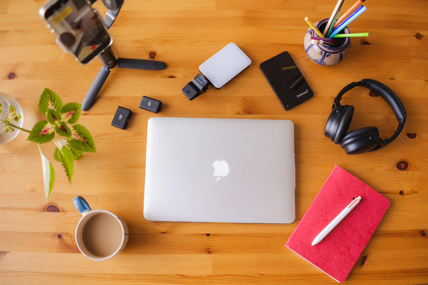 Laptop, Tasse, Notizheft, Kopfhörer, externe Festplatte, Handy & Stativ auf einem Schreibtisch